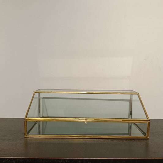 Glass display case with gold frame on a dark surface against a beige wall